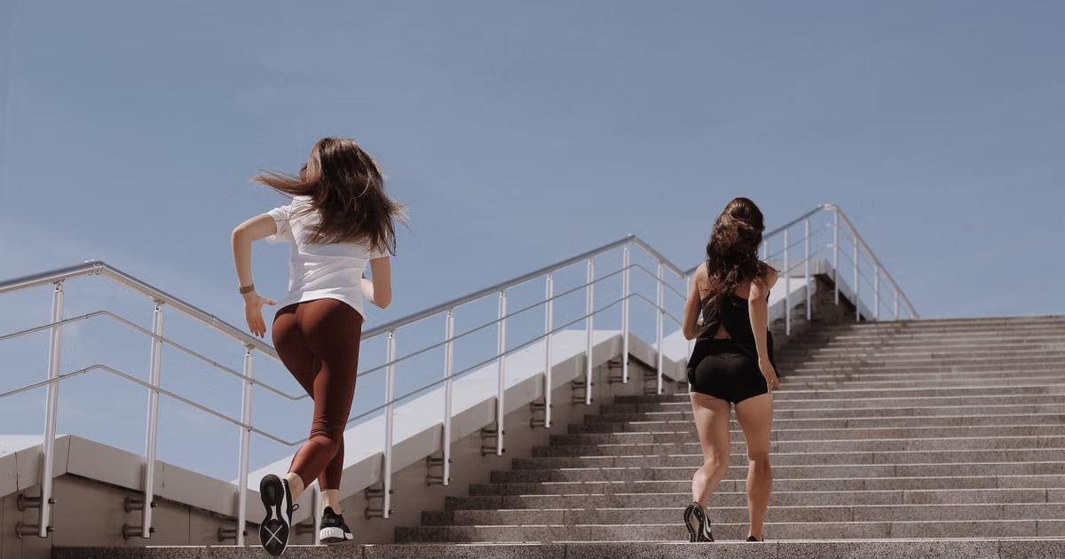 Two women running up outdoor stairs for fitness under a clear blue sky.